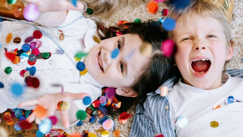 Kaksi lasta makaamassa lattialla nauraen ja heittäen värikästä konfettia ylleen.