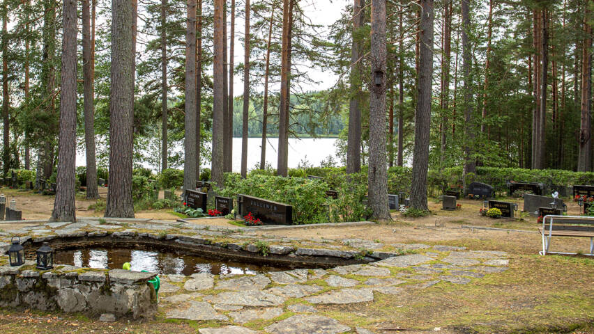 Ahvensalmen hautausmaa kesällä. Etualalla pieni vesiallas tai koristelampi. Taaempana hautoja ja kaukana taustalla näkyy järvi, jonka rannalla hautausmaa sijaitsee.