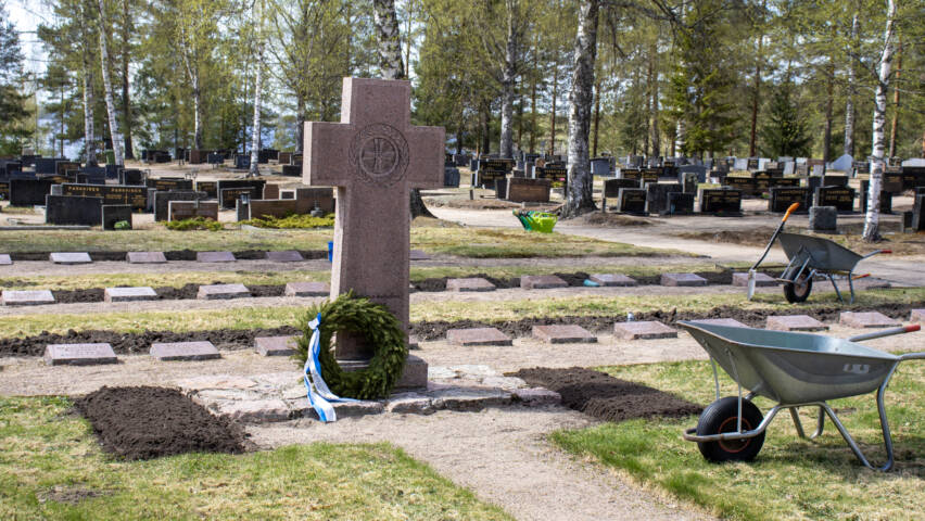 Sankarimuistomerkki keskellä sankarihautoja. Muistomerkin juurelle laskettu seppele sinivalkoisella nauhalla koristeltuna.