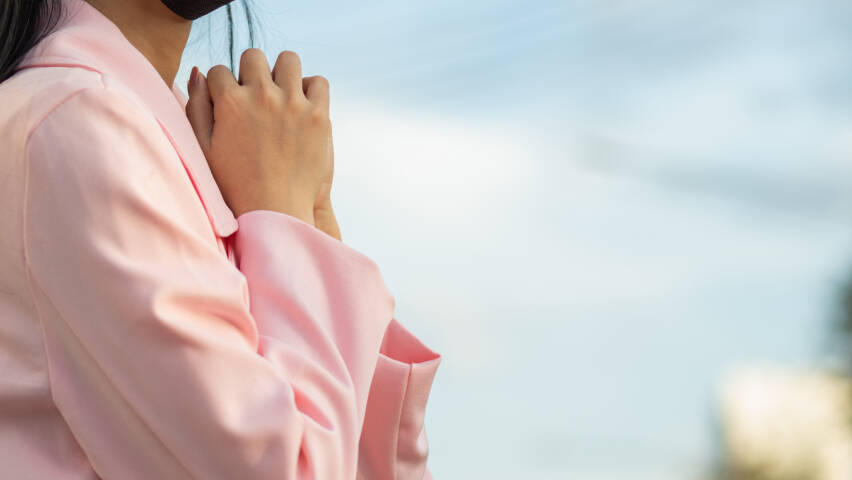A girl wearing a pink coat is standing praying.